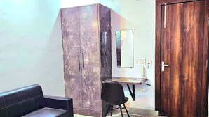 A room with a black leather sofa, a desk with a chair, a wardrobe, and a wooden door. - Hotel MoonLit (Noida)