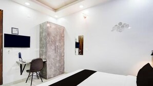 A modern hotel room with a bed, a desk, a chair, a wardrobe, and a TV mounted on the wall. - Hotel MoonLit (Noida)
