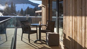 A wooden deck with a glass balustrade, a table with chairs, and a mountain view. - Luxurious apartment on the golf course (Westendorf)