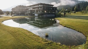 Un edificio moderno reflejado en un estanque, rodeado por un campo de golf y montañas.