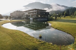 Ein modernes Gebäude mit Spiegelung in einem Teich, umgeben von einem Golfplatz und Bergen.