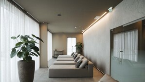 Un área de espera moderna con una hilera de sofás y una planta grande en maceta.