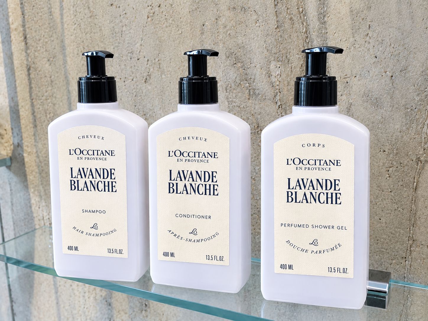 Trois bouteilles de produits L'Occitane en Provence sont posées sur une étagère en verre.