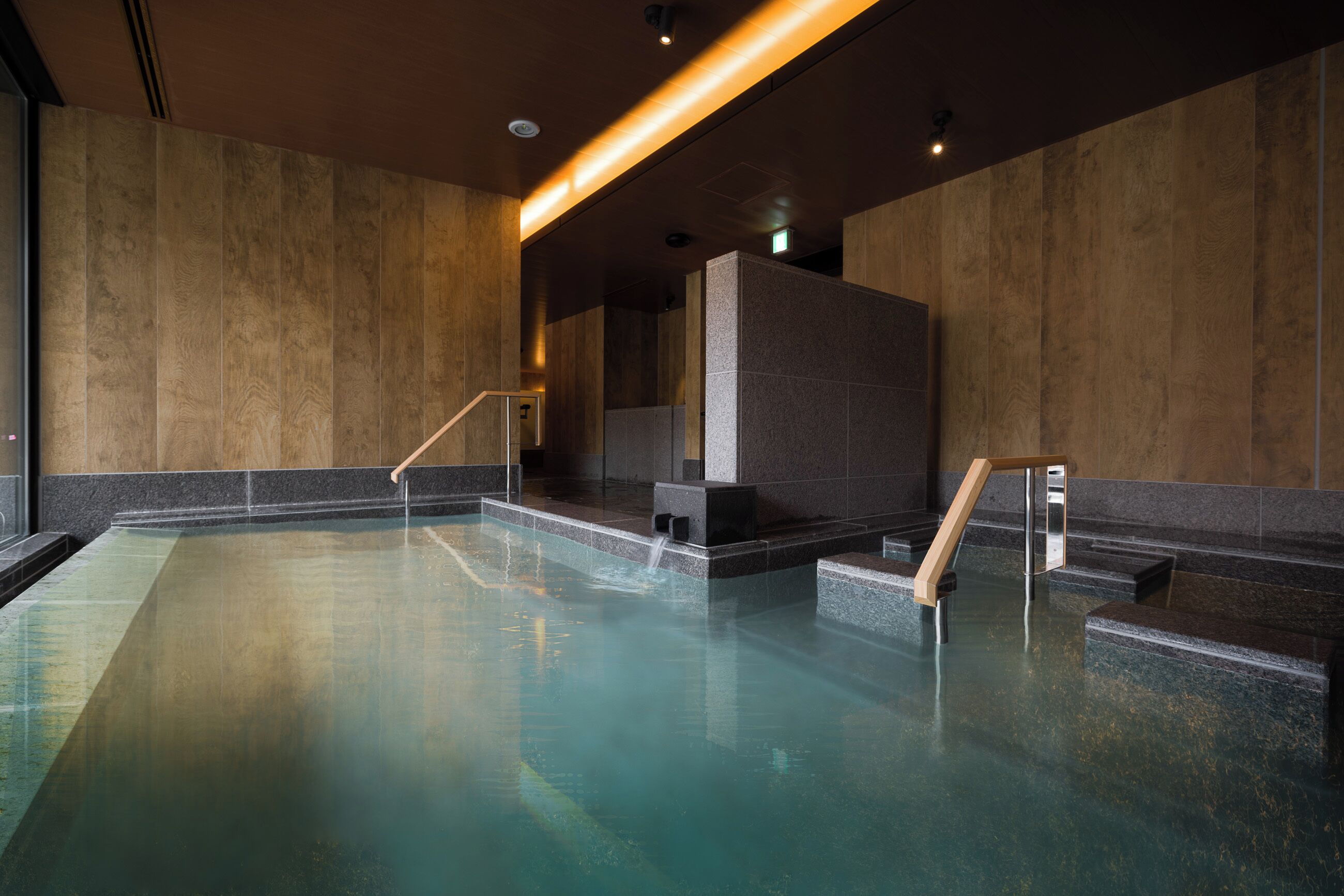 Ein moderner Innenpool mit Holzboden, Steinwänden und einer Holztreppe, die ins Wasser führt.