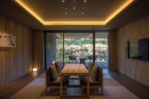 A modern dining area with a wooden table and chairs, a large window offering a view of a forested hillside, and a flat-screen TV mounted on the wall. - Kinugawa Keisui (Nikko)