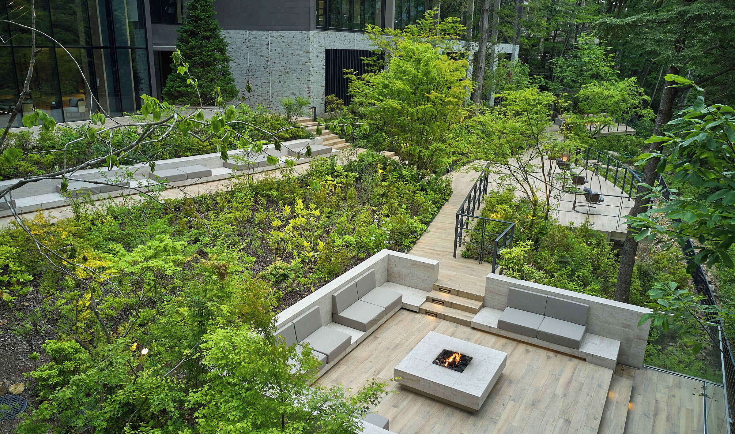A rooftop garden with a fire pit, seating areas, and a staircase leading to a building.