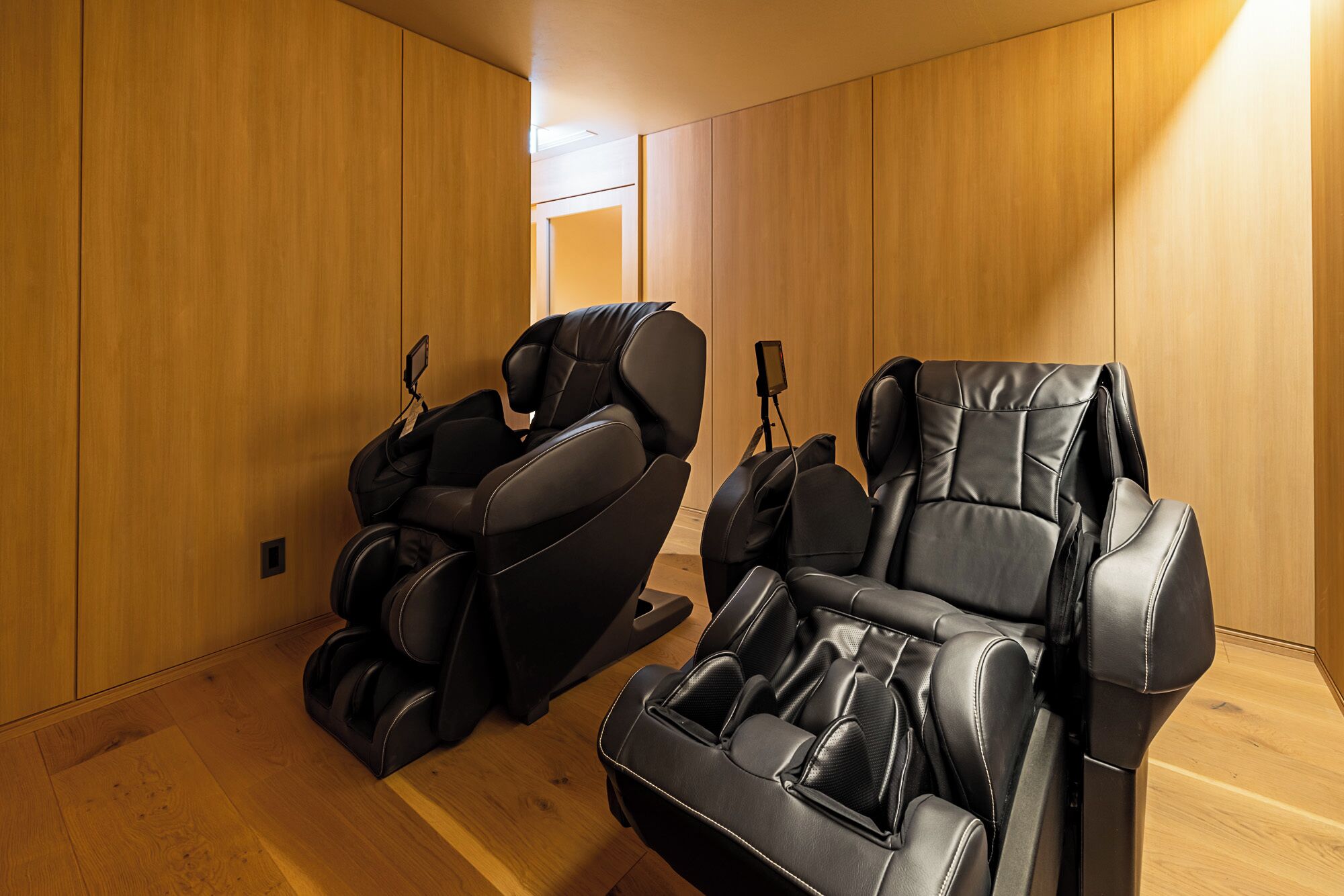 A room with two massage chairs and wooden panel walls.