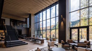 Eine großzügige Lobby mit modernem Design, inklusive Treppe, Sitzgelegenheit und großen Fenstern mit Blick auf Herbstlaub.