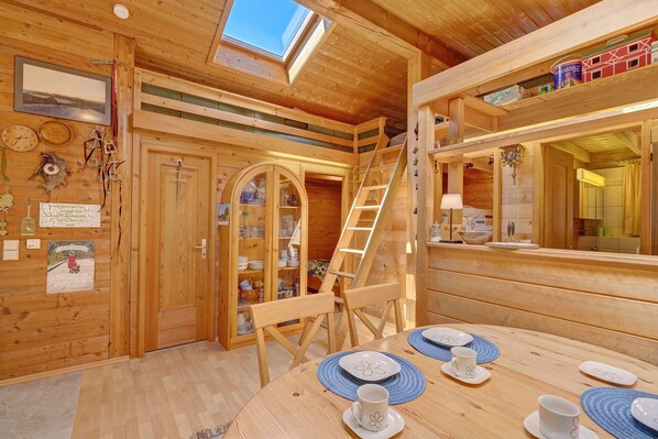 A wooden interior with a dining table set for two, a ladder, and a skylight.