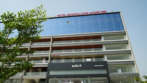A hotel with a modern glass facade, a Kia dealership below, and a sign for 'Hotel Bhagyalaxmi Luxury Inn' at the top. - HOTEL BHAGYALAXMI LUXURY INN (Gandhinagar)