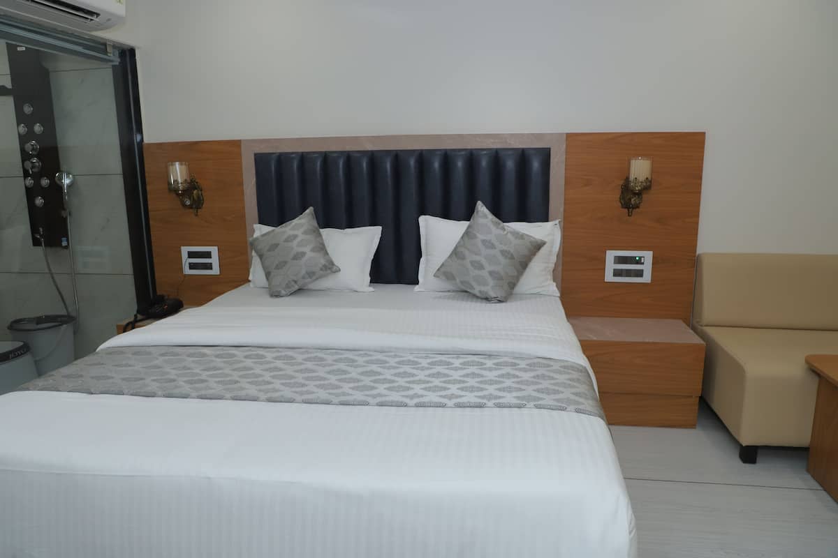 A hotel room with a large bed, a wooden headboard, two bedside tables with lamps, a small seating area, and a shower.