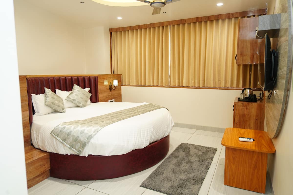 A hotel bedroom with a large bed, a wooden headboard, a TV mounted on the wall, and a small wooden side table.