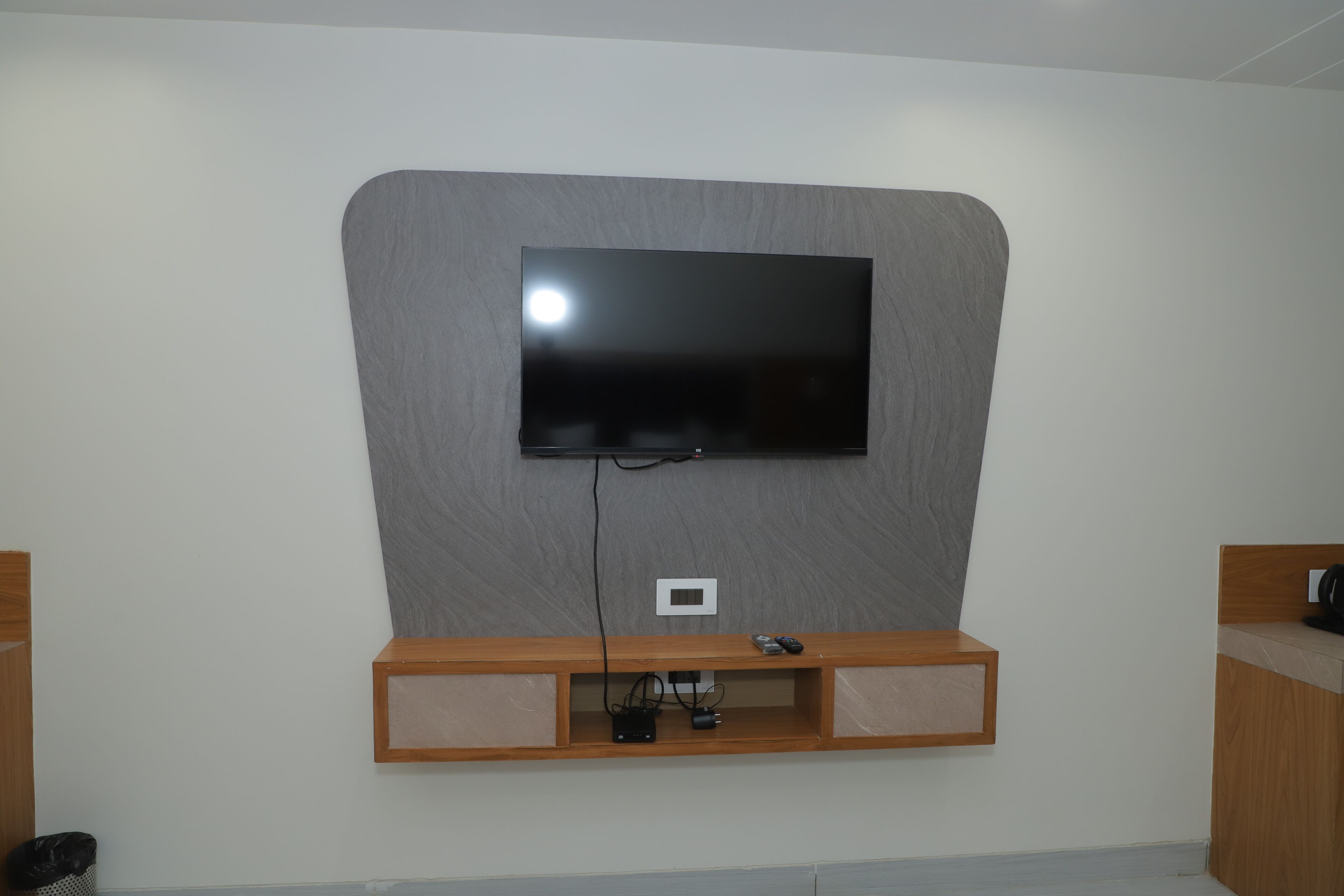A modern room with a mounted flat-screen TV, wooden entertainment unit, and a small white switchboard.