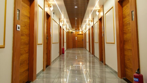 A long, well-lit hallway with wooden doors and a fire extinguisher on the right. - HOTEL BHAGYALAXMI LUXURY INN (Gandhinagar)