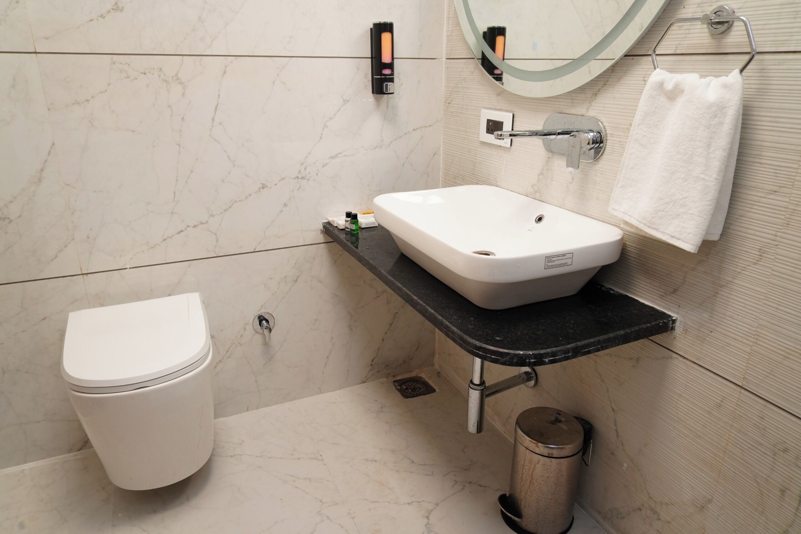 A bathroom with a white toilet, a white sink with a black countertop, a mirror, and a towel rack.