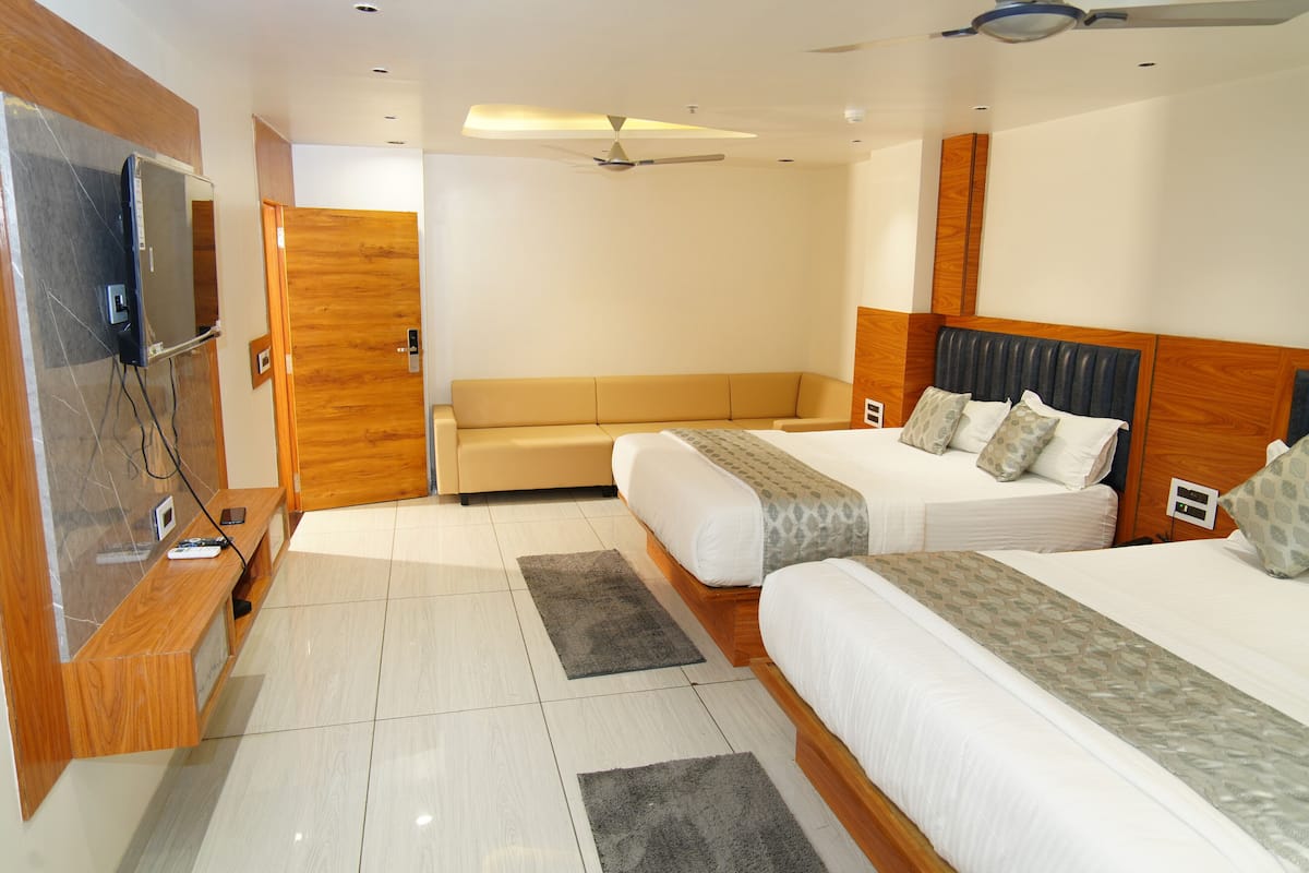 A hotel room with two beds, a sofa, a TV, and a ceiling fan.