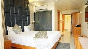 A modern hotel room with a large bed, wooden headboard, air conditioning unit, and a small desk with a chair. - HOTEL BHAGYALAXMI LUXURY INN (Gandhinagar)