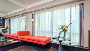 Et moderne hotelværelse med en rød sofa, et rundt glastbord med en bærbar computer og en vase med blomster.