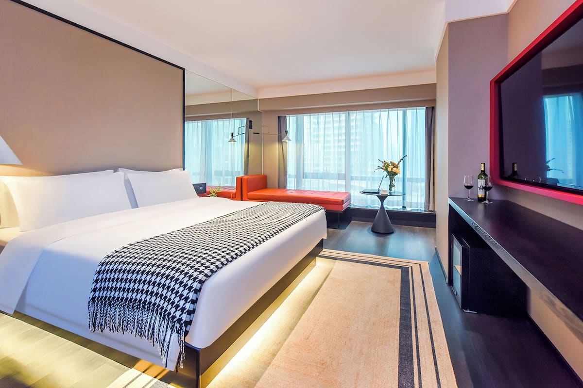 Ein modernes Hotelzimmer mit einem großen Bett, einer Sitzecke mit einem roten Sofa, einem kleinen Tisch mit Blumen und einem an der Wand befestigten Fernseher.