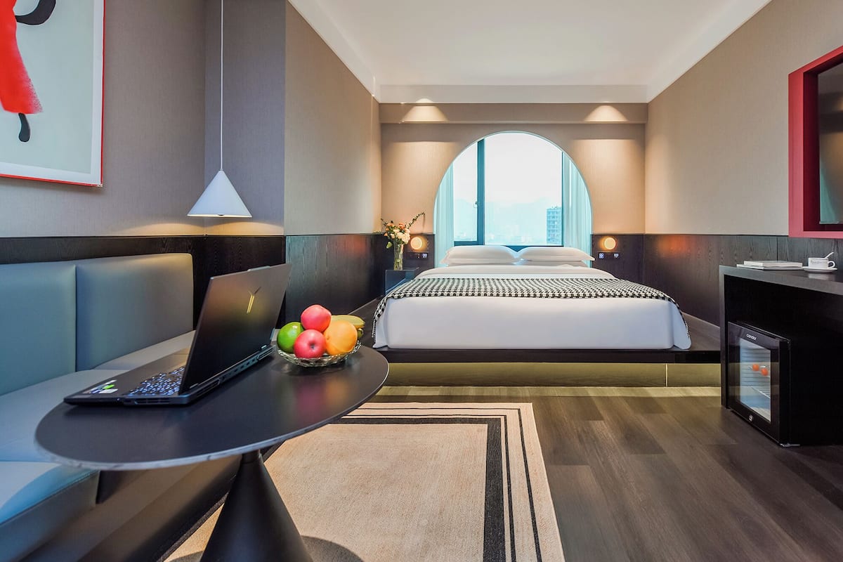 Ein modernes Hotelzimmer mit einem Bett, einem Laptop auf einem Tisch und einer Obstschale.