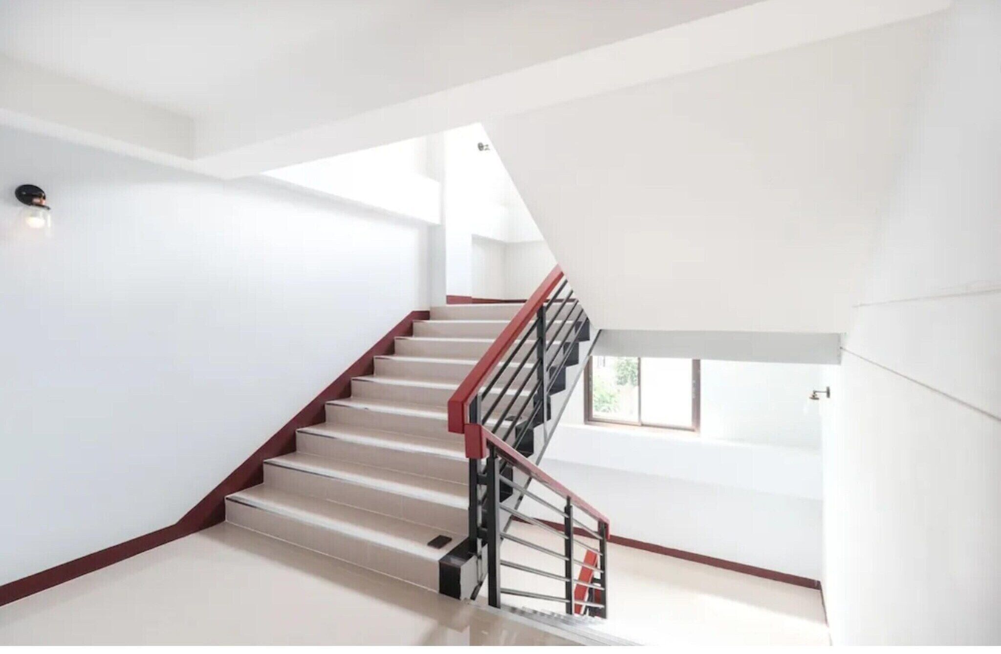 Un escalier moderne avec une rampe rouge et des balustres noires, menant à l’étage supérieur.