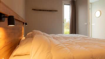 Een net opgemaakt bed met een houten hoofdeinde en bedlampjes, een raam met gordijnen, en een deur met een ronde spiegel.