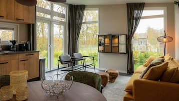 Een moderne keuken met grote ramen, een eethoek met een ronde tafel, en een gezellige woonkamer met een bank en poufs.