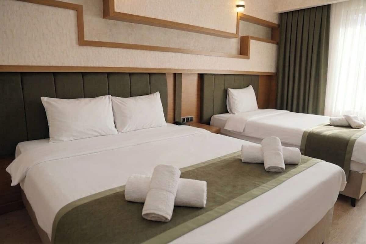 Habitación de hotel con dos camas, cabecero, luz de pared y ventana con cortinas.