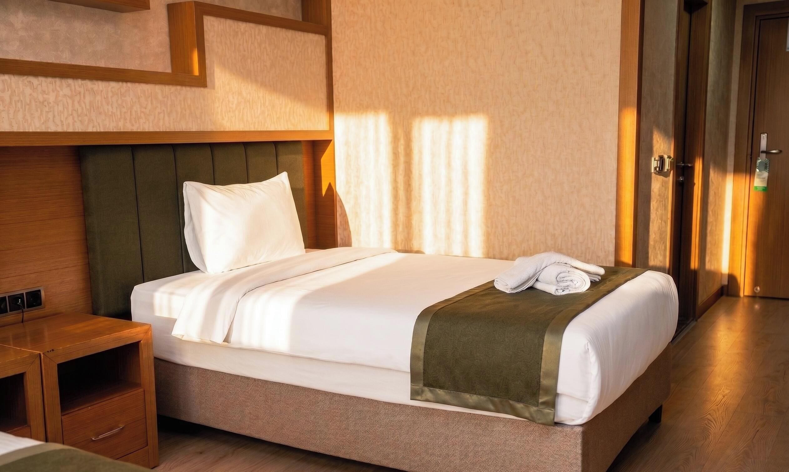 Ein Hotelzimmer mit Bett, Nachttisch, Holztür und Wand mit strukturierter Oberfläche.