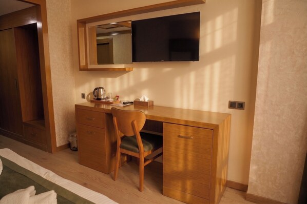 A hotel room with a wooden desk, chair, and a flat-screen TV mounted above it.