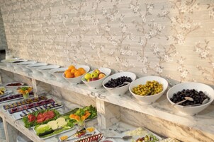 Buffet com diversos alimentos e um painel floral ao fundo.
