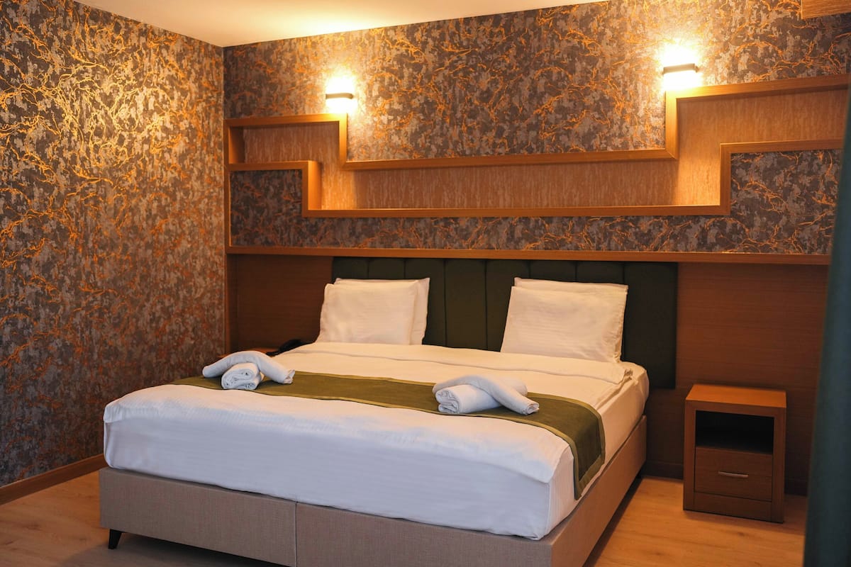 Una habitación de hotel con una cama grande, dos mesitas de noche y una pared con un diseño textural único.