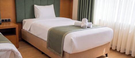 Une chambre d’hôtel avec un lit, une table de chevet, une tête de lit verte et une fenêtre avec des rideaux.
