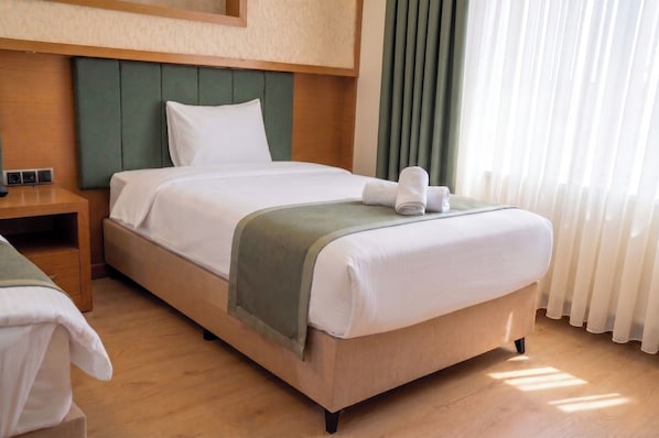 Ein Hotelzimmer mit Bett, Nachttisch, grünem Kopfteil und einem Fenster mit Vorhängen.