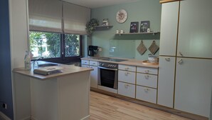 Una cocina con estufa, horno y pileta, muebles de madera y una ventana que da a vista de árboles.