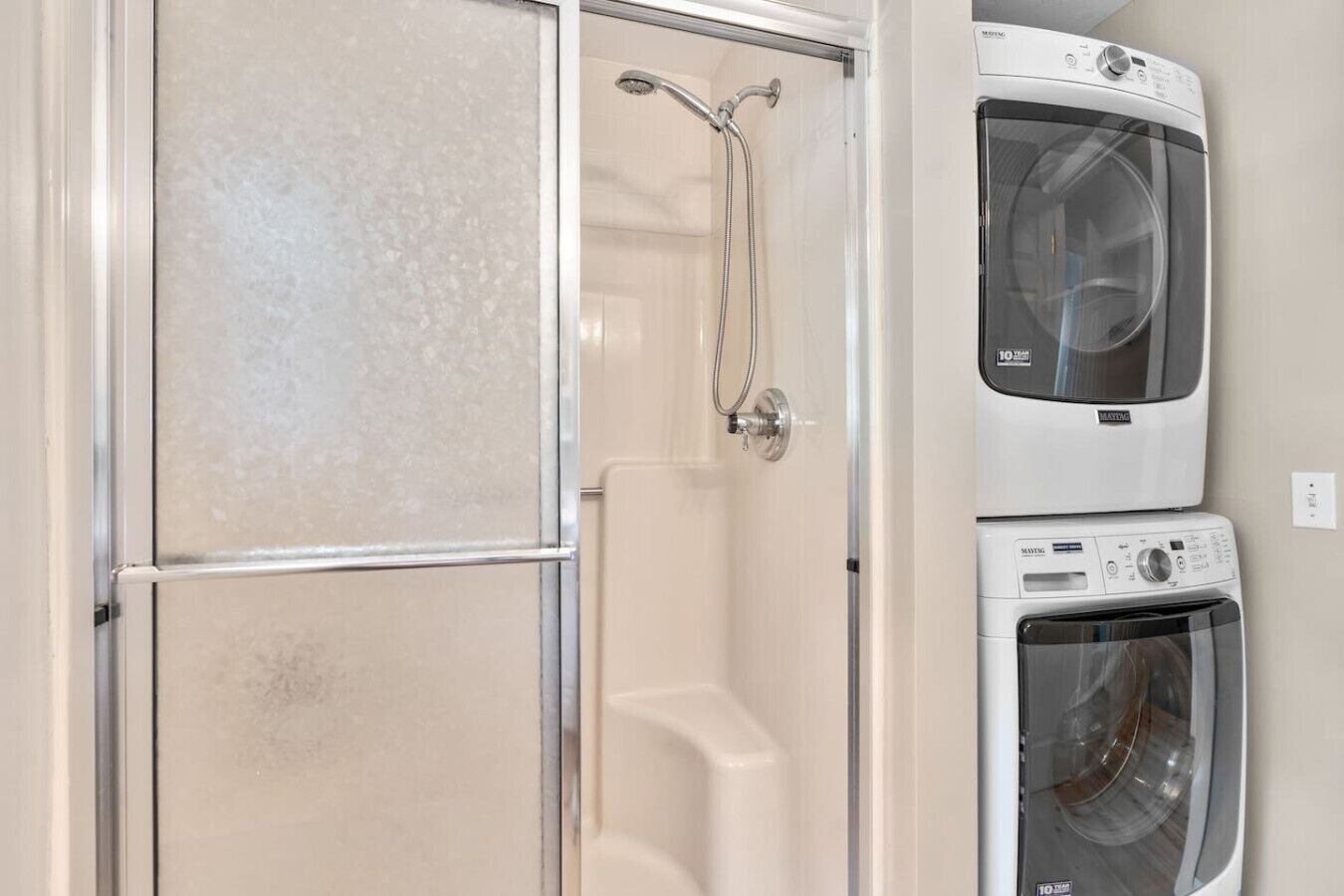 Un baño con cabina de ducha de vidrio, una bañera blanca y lavadoras apiladas.