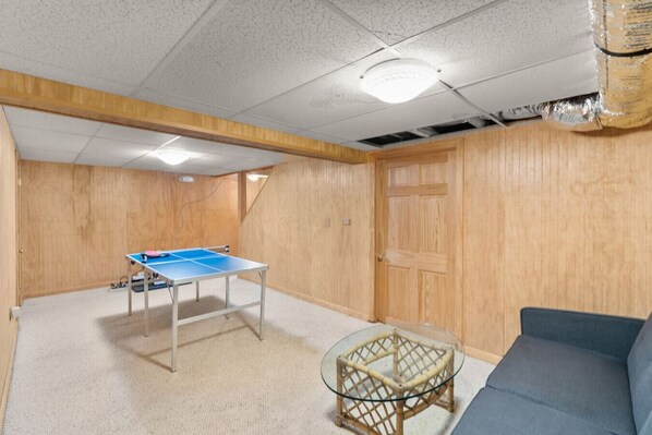 A room with a ping pong table, a glass coffee table, and a blue sofa.