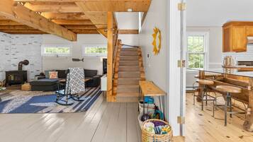 A cozy cabin interior with a wooden staircase, a living area with a sofa and a fireplace, and a kitchen with wooden bar stools.