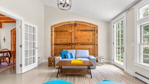 A spacious living room with a large wooden door, a grey sofa with blue cushions, and a yellow tray on the coffee table. - Gorgeous Home 1 mile to Beach, by Cape Cod Bikepath (Dennis)