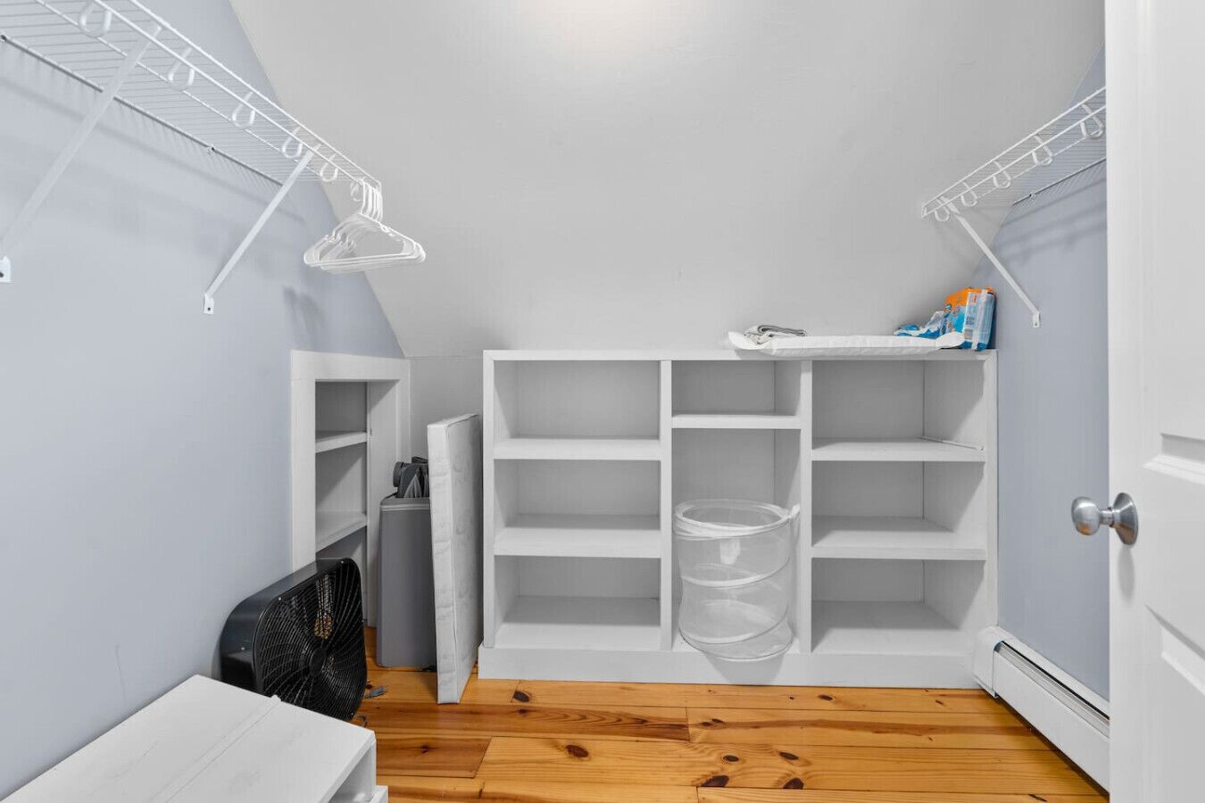 A small, narrow hallway with white shelving units and a clear plastic storage bin.