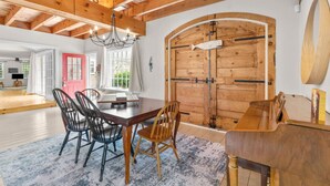 A spacious dining area with a wooden table and chairs, a chandelier, and a large wooden door. - Gorgeous Home 1 mile to Beach, by Cape Cod Bikepath (Dennis)