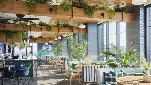 An indoor dining area with wooden tables and chairs, surrounded by large windows and potted plants. - Pink Dreams - Walk to Live Music, Bars, Restaurants - Free Parking (Nashville)