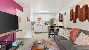 A compact living space with a kitchen, a grey sofa, a coffee table, and a TV on a stand. - Pink Dreams - Walk to Live Music, Bars, Restaurants - Free Parking (Nashville)