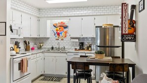 A compact kitchen with white cabinets, a stainless steel range, and a dining area with a table and chairs. - Pink Dreams - Walk to Live Music, Bars, Restaurants - Free Parking (Nashville)