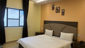 Une chambre d’hôtel comprenant un lit, une table de chevet, une commode, une fenêtre avec des rideaux et des tableaux accrochés au mur.