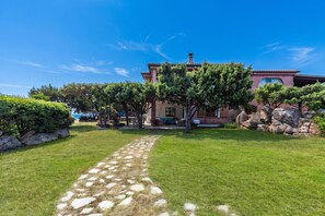 A house with a paved pathway leading to the entrance, surrounded by well-maintained grass and trees. - Casa Ortensia Apartments (Arzachena)