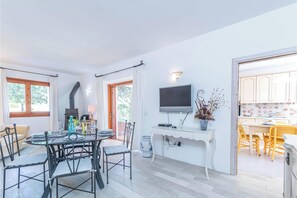 Un coin repas avec une table ronde, des chaises et un téléviseur posé sur un meuble blanc.