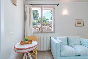 A room with a white radiator, a wicker table with a small plant, a striped sofa, and a window with curtains.