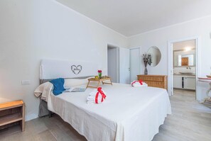 A hotel room with a neatly made bed, a bedside table with a vase of flowers, a mirror, and a view into the bathroom.