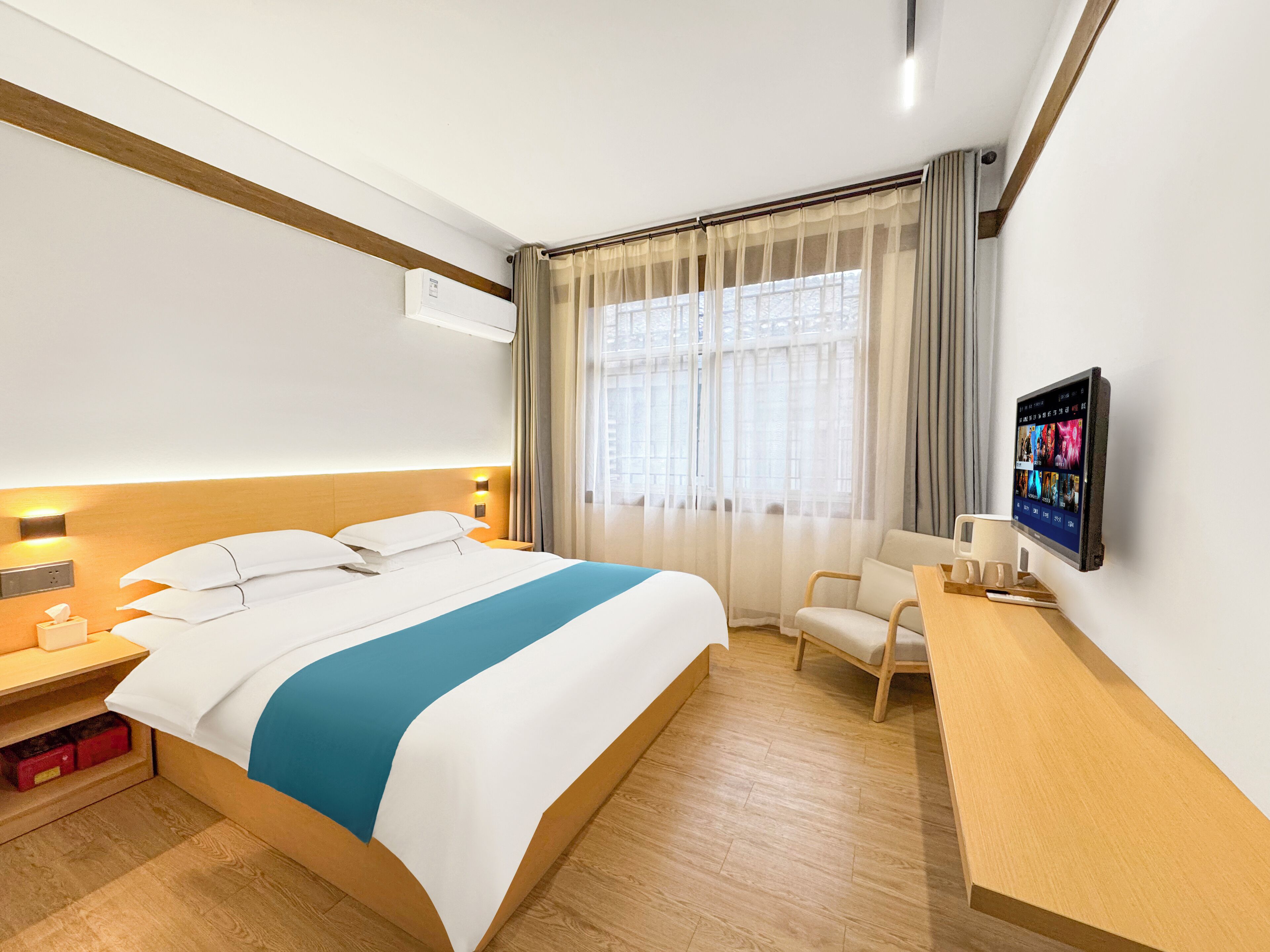 Une chambre d’hôtel avec un grand lit, un bureau doté d’un téléviseur à écran plat, une chaise et une fenêtre ornée de rideaux légers.